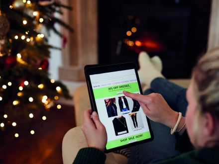 Woman At Home Using Digital Tablet To Shop For Clothes Online At Christmas
