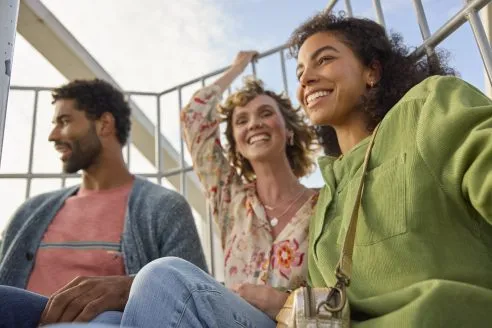 Two female models and a male model wearing colourful FatFace clothing from its Spring 25 collection on a ferris wheel.
