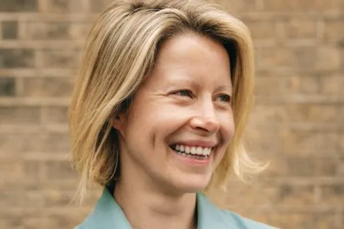 TFG London chief brand officer Julia Monro, a smiling woman with short blonde hair, standing in front of brick wall