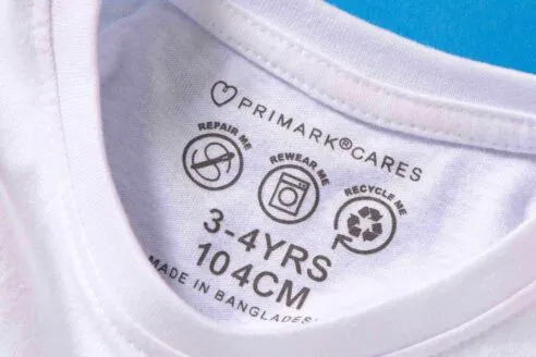 A close-up of the product information graphic on the back lining of a white t-shirt for children of 3-4 years, showcasing Primark's shift away from neck labels