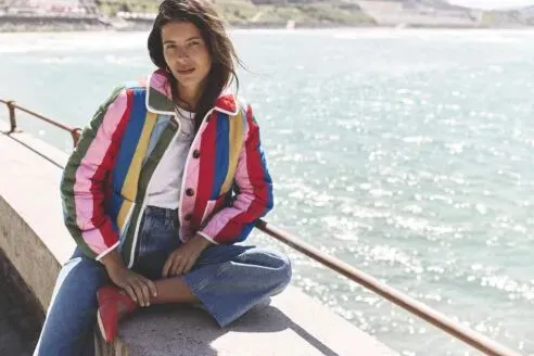Model wearing colourful jacket over white tshirt and jeans on boat on water