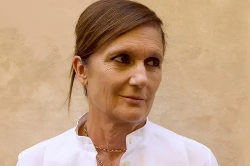 Maria Grazia Chiuri looking to the right wearing white shirt standing against yellow-beige wall